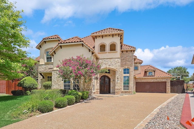 mediterranean / spanish home with stucco siding, fence, a garage, stone siding, and driveway