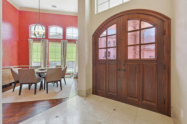 entrance foyer featuring light tile patterned flooring, crown molding, a high ceiling, baseboards, and an inviting chandelier