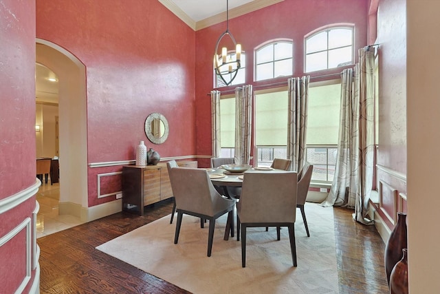 dining space with ornamental molding, arched walkways, a chandelier, and wood finished floors