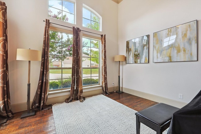 sitting room featuring baseboards, a high ceiling, dark wood finished floors, and a healthy amount of sunlight