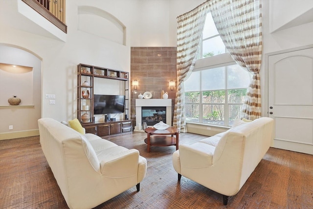 living area featuring a large fireplace, a high ceiling, wood finished floors, and baseboards