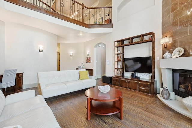 living area featuring arched walkways, a large fireplace, a towering ceiling, and baseboards