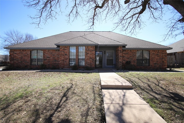 ranch-style home with roof with shingles, a front lawn, and brick siding