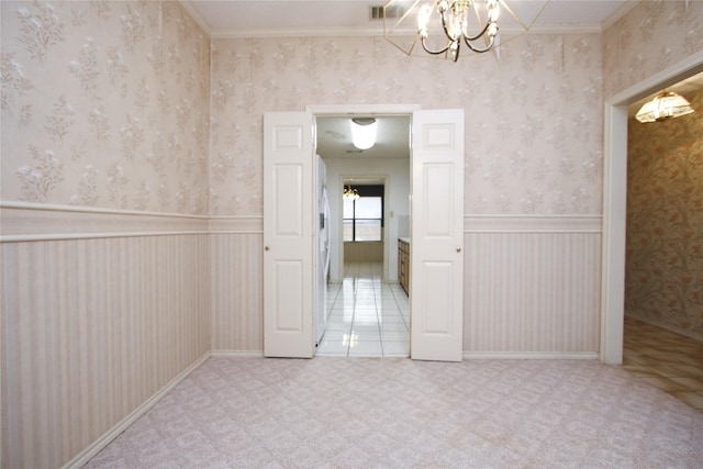 unfurnished room with wallpapered walls, an inviting chandelier, a wainscoted wall, and carpet flooring