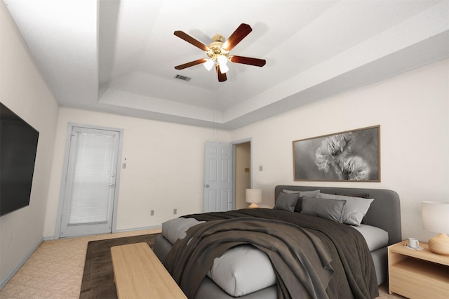 carpeted bedroom featuring baseboards, visible vents, a tray ceiling, and a ceiling fan