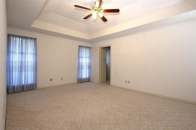 empty room featuring a ceiling fan, a raised ceiling, light carpet, and baseboards