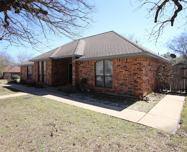 view of side of home with a yard, brick siding, and a shingled roof