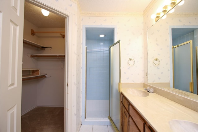 full bathroom with a textured ceiling, a sink, a stall shower, a walk in closet, and wallpapered walls