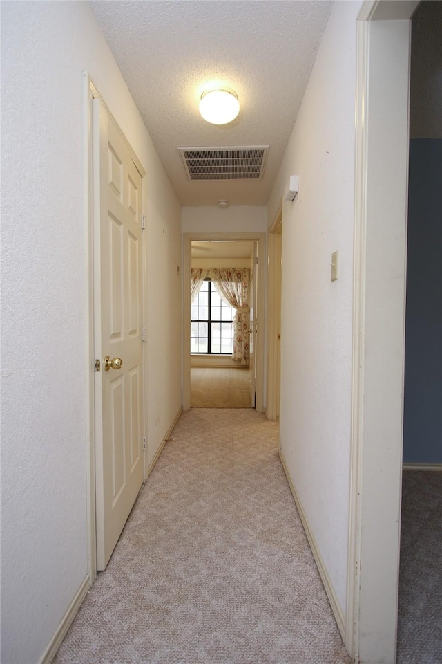 corridor featuring carpet floors, baseboards, visible vents, and a textured ceiling