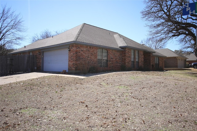 view of home's exterior with a garage, brick siding, fence, and roof with shingles