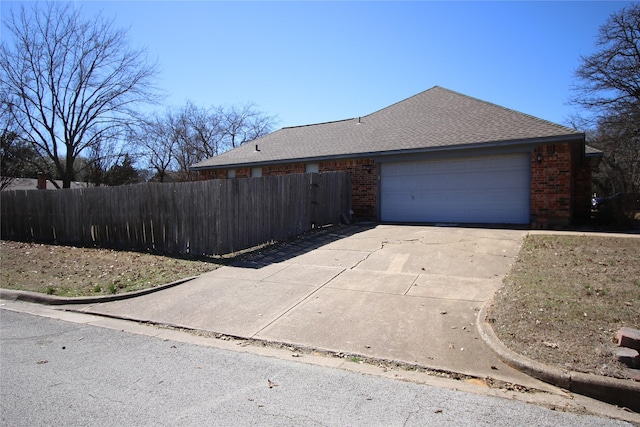 view of front facade featuring brick siding, roof with shingles, an attached garage, fence, and driveway