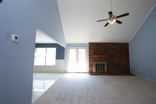 unfurnished living room featuring a ceiling fan, wainscoting, tile patterned floors, a brick fireplace, and high vaulted ceiling