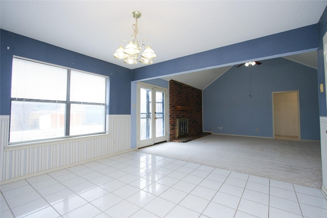 unfurnished living room with a wainscoted wall, lofted ceiling, a brick fireplace, carpet flooring, and tile patterned floors