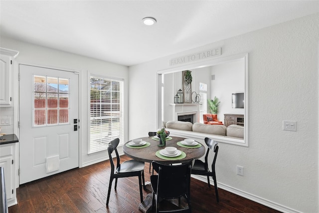 dining space with dark wood-style floors, a fireplace, and baseboards