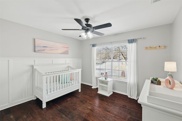 bedroom featuring ceiling fan, a crib, wainscoting, and wood finished floors