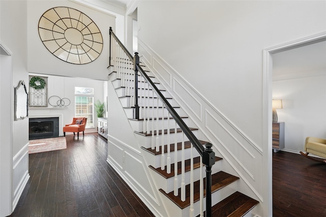 staircase featuring wood-type flooring, a fireplace, a towering ceiling, and baseboards