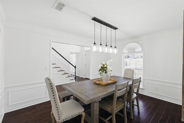 dining room with dark wood-style floors, visible vents, crown molding, and a decorative wall