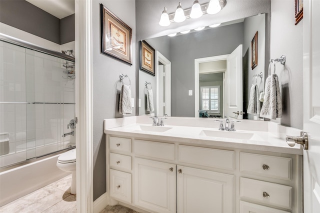 bathroom featuring double vanity, shower / bath combination with glass door, toilet, and a sink