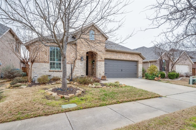 french country inspired facade with a garage, concrete driveway, stone siding, roof with shingles, and brick siding