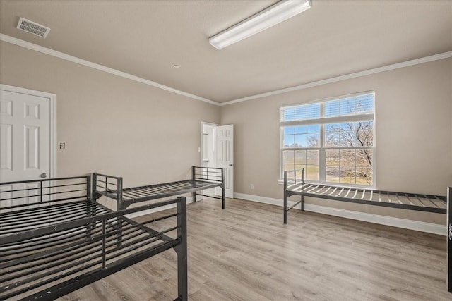 bedroom featuring light wood-style floors, baseboards, visible vents, and crown molding