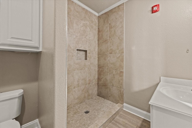 bathroom with baseboards, tiled shower, toilet, crown molding, and vanity