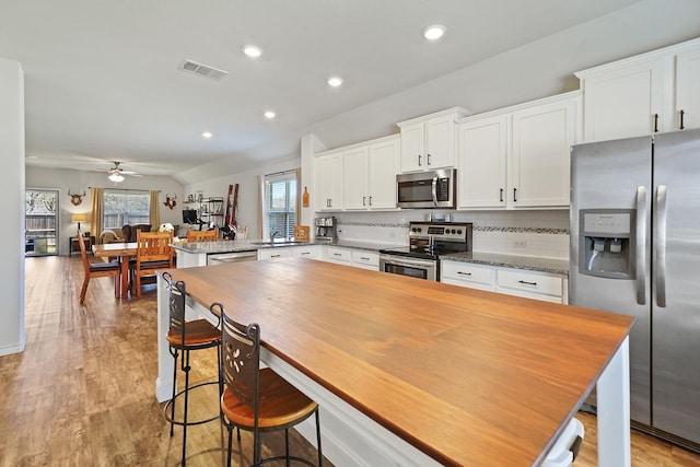 kitchen with appliances with stainless steel finishes, light wood-type flooring, a peninsula, and tasteful backsplash