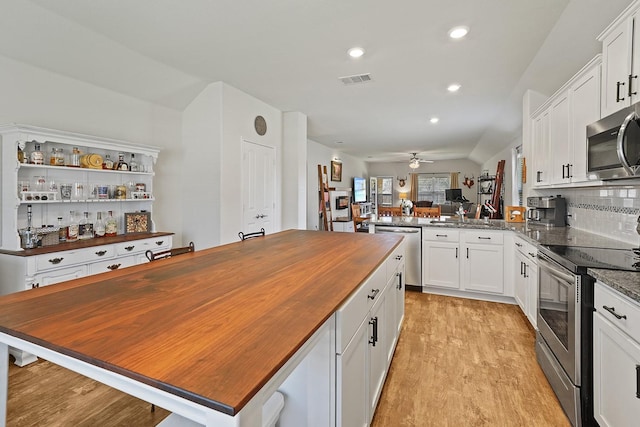 kitchen with light wood finished floors, backsplash, appliances with stainless steel finishes, white cabinetry, and butcher block countertops