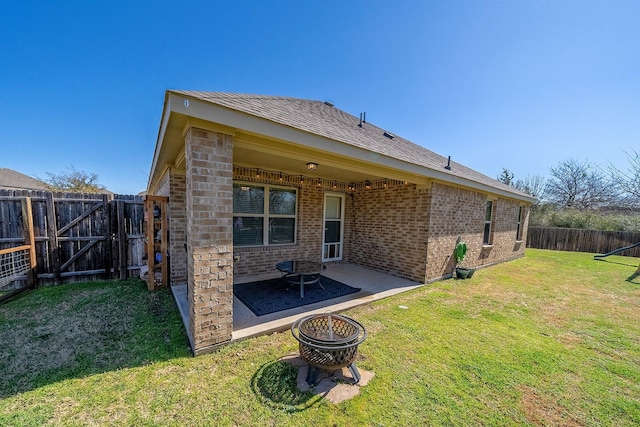 back of house with brick siding, a yard, a patio, an outdoor fire pit, and a fenced backyard