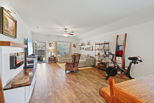 living area featuring visible vents, a ceiling fan, a glass covered fireplace, lofted ceiling, and wood finished floors