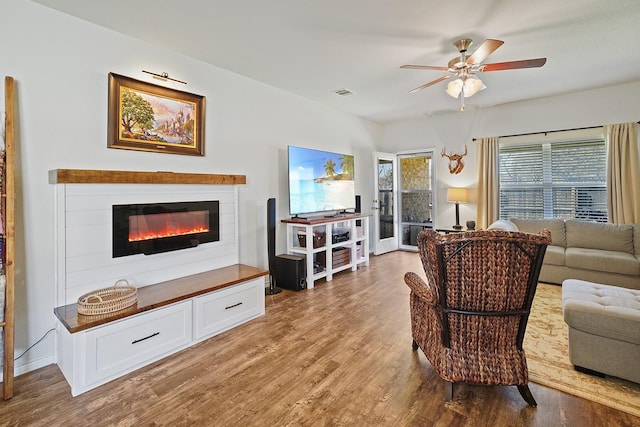 living room featuring ceiling fan, visible vents, wood finished floors, and a glass covered fireplace