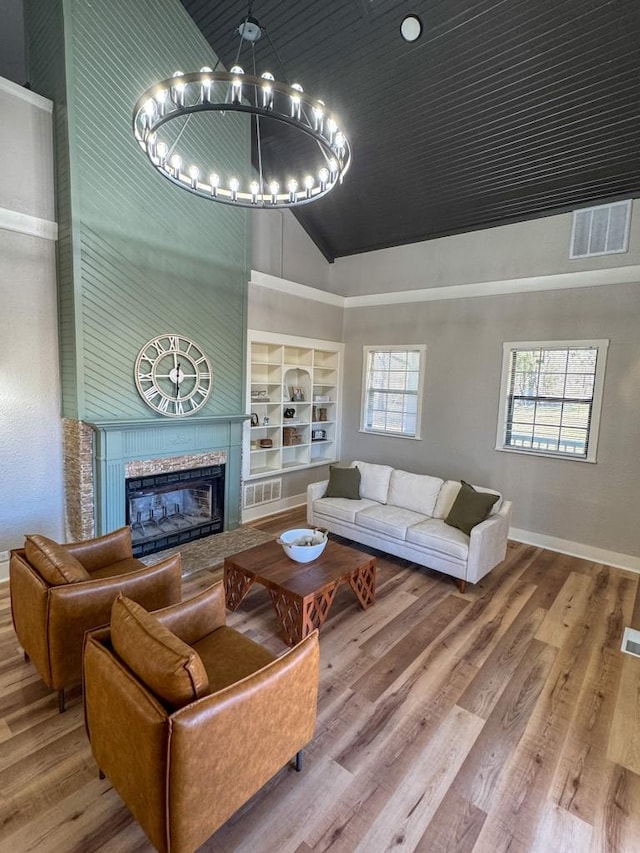 living room with wood finished floors, visible vents, baseboards, built in features, and a glass covered fireplace