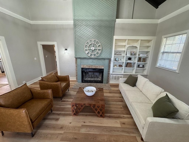 living room with built in shelves, a fireplace, a towering ceiling, wood finished floors, and baseboards