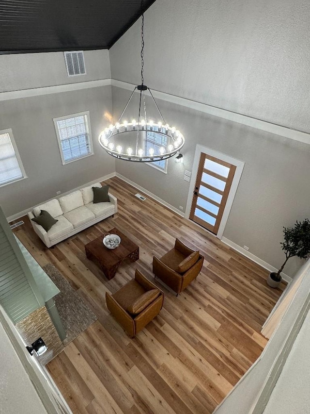 unfurnished living room featuring a notable chandelier, wood finished floors, visible vents, baseboards, and vaulted ceiling