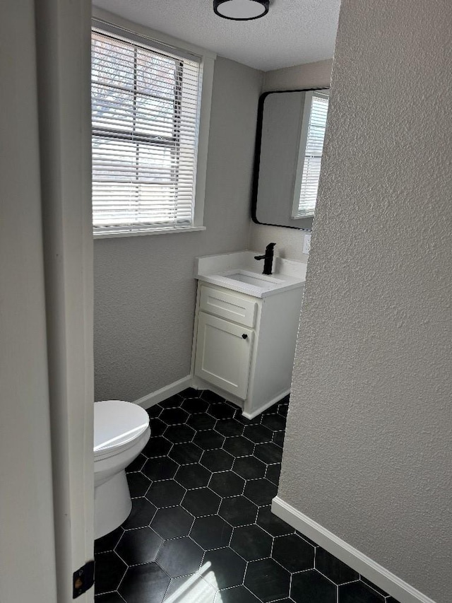 bathroom with toilet, a textured wall, plenty of natural light, and vanity