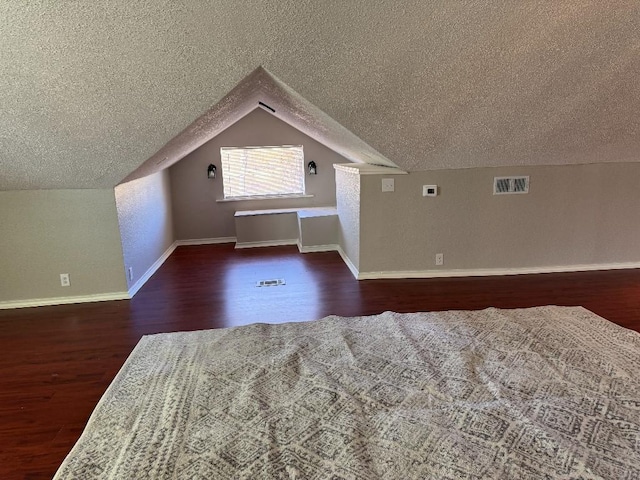 additional living space with baseboards, visible vents, lofted ceiling, dark wood-style floors, and a textured ceiling