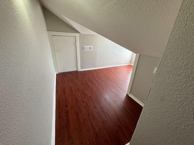 hall with visible vents, a textured wall, lofted ceiling, wood finished floors, and a textured ceiling