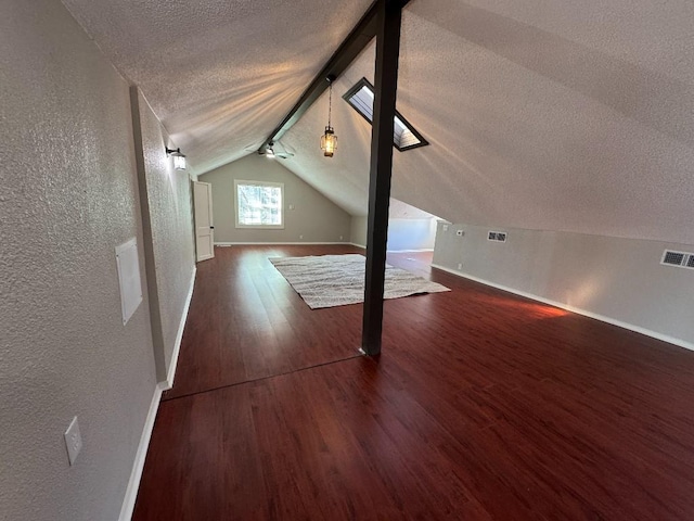 additional living space with a textured ceiling, a textured wall, vaulted ceiling with skylight, visible vents, and dark wood finished floors