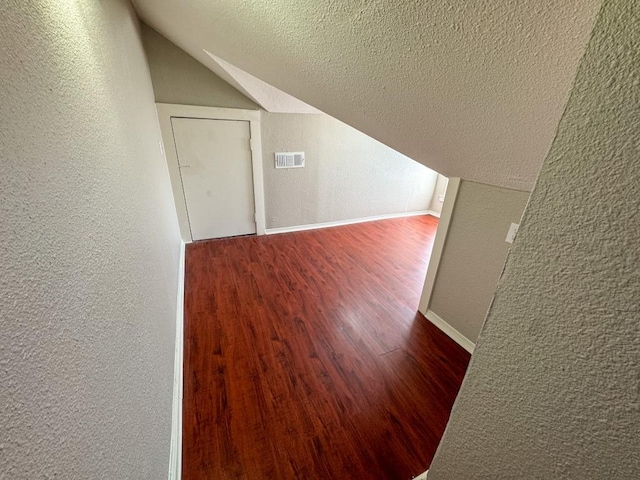 additional living space featuring a textured ceiling, a textured wall, lofted ceiling, wood finished floors, and visible vents