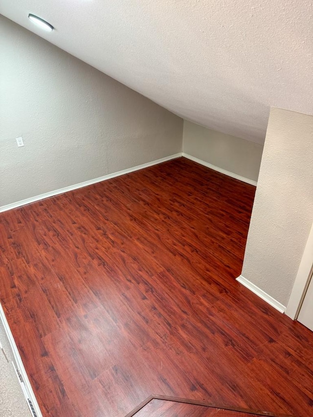 unfurnished room featuring lofted ceiling, a textured ceiling, baseboards, and wood finished floors