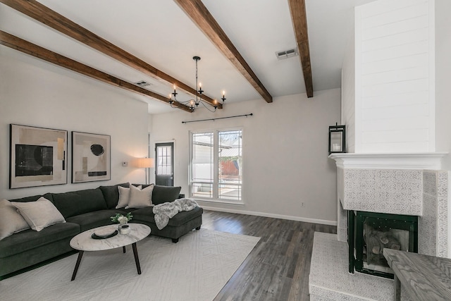 living area with visible vents, a tiled fireplace, wood finished floors, beamed ceiling, and baseboards