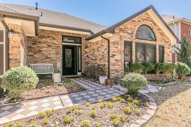 view of exterior entry featuring roof with shingles and brick siding