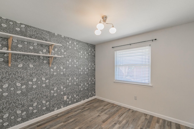 unfurnished room featuring an inviting chandelier, wood finished floors, baseboards, and wallpapered walls