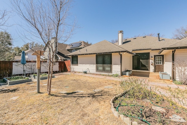 back of house featuring a chimney, fence, a vegetable garden, and roof with shingles