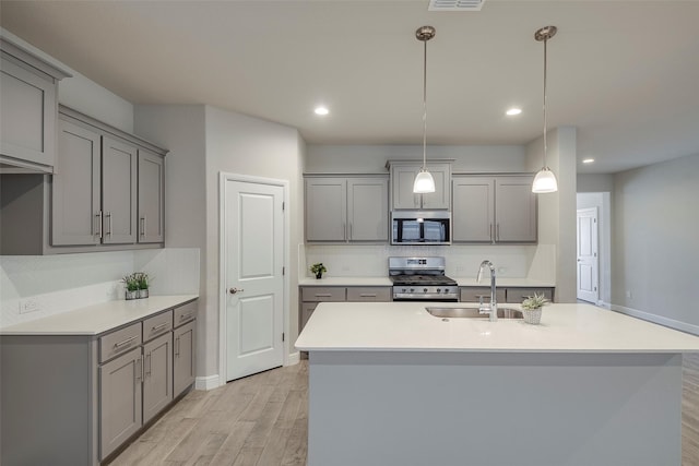 kitchen featuring light wood finished floors, a sink, gray cabinetry, light countertops, and appliances with stainless steel finishes