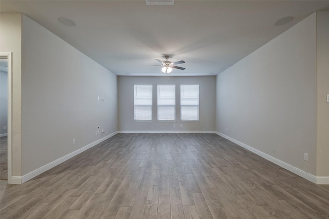 spare room with ceiling fan, visible vents, baseboards, and wood finished floors