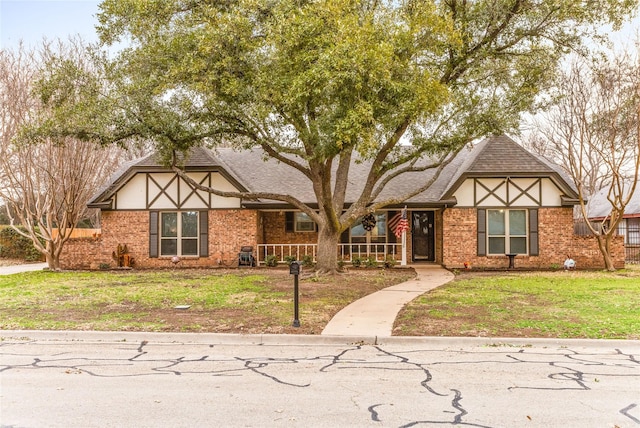 tudor house with roof with shingles, brick siding, a front lawn, and a porch