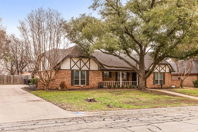 tudor home featuring a porch, brick siding, fence, and a front lawn