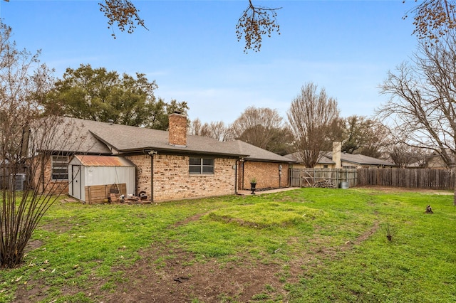 rear view of property with a storage shed, a chimney, fence, a yard, and brick siding