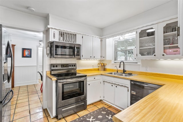 kitchen featuring a wainscoted wall, a sink, white cabinetry, ornamental molding, and appliances with stainless steel finishes