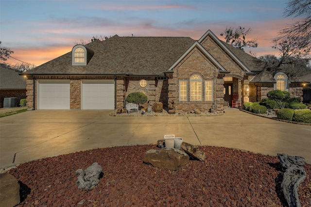 view of front of property featuring a garage, a shingled roof, concrete driveway, central AC, and brick siding